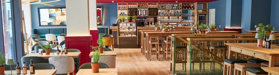Innenaufnahme vom VAPIANO Hamburg Gänsemarkt mit Tischen, Stühlen und der Bar im Hintergrund.