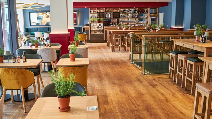 Innenaufnahme vom VAPIANO Hamburg Gänsemarkt mit Tischen, Stühlen und der Bar im Hintergrund.