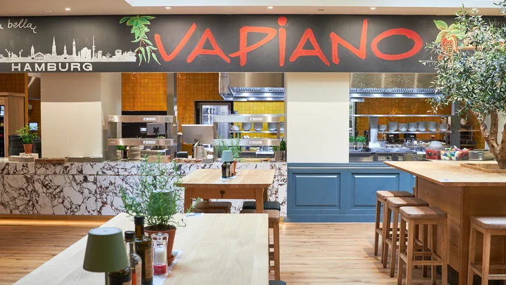 Innenaufnahme vom VAPIANO Hamburg Gänsemarkt mit Tischen, Stühlen und der Theke zum Bestellen im Hintergrund.