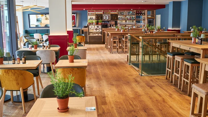 Innenaufnahme vom VAPIANO Hamburg Gänsemarkt mit Tischen, Stühlen und der Bar im Hintergrund.