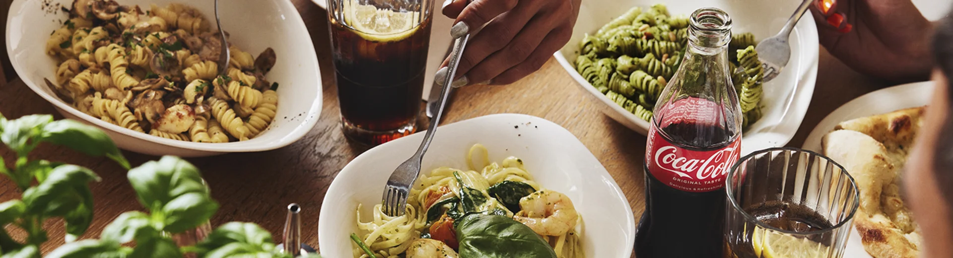 Personen essen verschiedene Pasta-Gerichte am gedeckten Tisch mit Getränken.