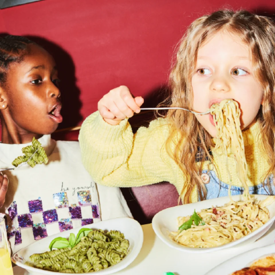 Zwei Kinder sitzen im Restaurant und essen Pasta.