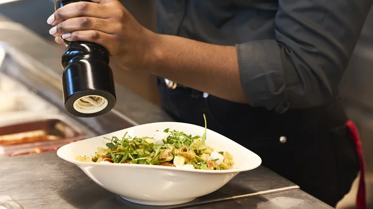 Eine Köchin würzt in der Küche ein Pasta-Gericht.