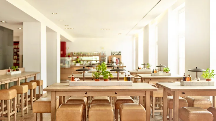 Innenaufnahme vom VAPIANO Mannheim mit Tischen, Hockern und frischen Kräutern.