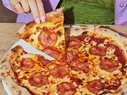 Eine Person hält ein Stück von einer Salami Pizza.