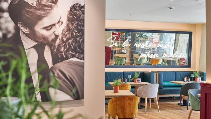 Innenaufnahme vom VAPIANO Hamburg Gänsemarkt mit einem dekorativen Foto an der Wand und einem Spiegel über den Sitzmöglichkeiten im Hintergrund.