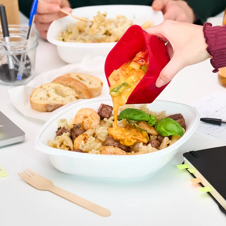 Sauce wird aus einem Behälter über die Pasta gegossen.