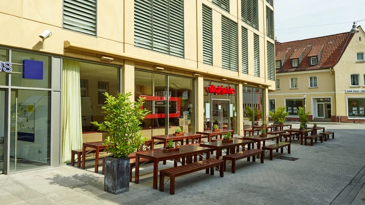 Außenansicht vom VAPIANO Osnabrück mit Bänken, Tischen und Pflanzen im Außenbereich.