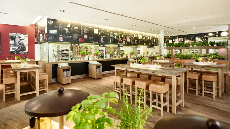 Innenaufnahme vom VAPIANO Osnabrück mit Sitzmöglichkeiten und der Theke zum Bestellen im Hintergrund.