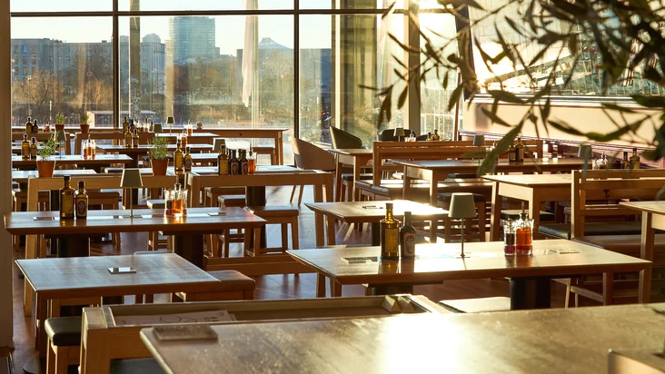 Innenaufnahme vom VAPIANO Berlin Europaplatz mit Tischen und Stühlen vor großen Fenstern.
