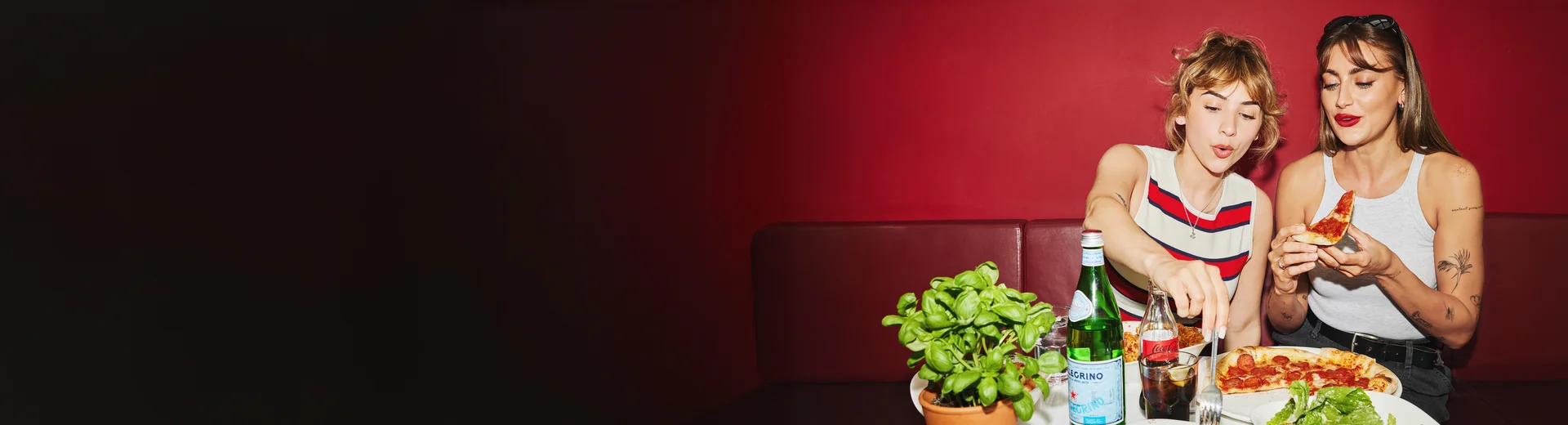 Zwei Frauen sitzen im Restaurant und essen Pasta und Pizza.