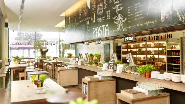 Innenaufnahme vom VAPIANO Hamburg Kurze Mühren mit Tischen, Stühlen und der Theke zum Bestellen im Hintergrund.
