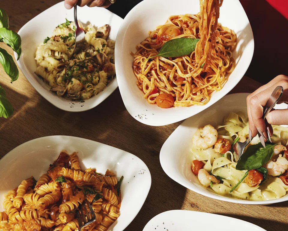 Personen essen verschiedene Pasta-Gerichte am gedeckten Tisch.