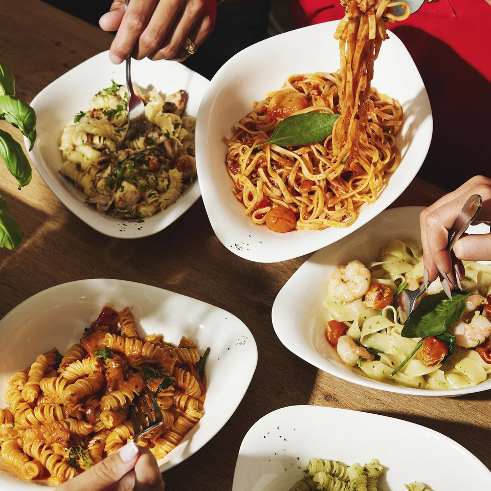Personen essen verschiedene Pasta-Gerichte am gedeckten Tisch.